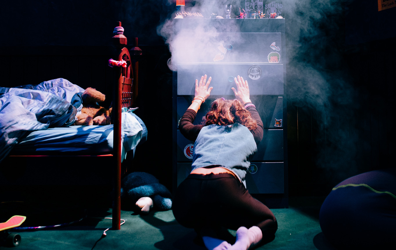 Une actrice est de dos, sur les genoux. Elle essaie de refermer un tiroir d'une commode de laquelle sort de la fumée. Elle est dans une chambre, un lit est à côté d'elle. Des objets de toutes sortes trônent sur le meuble.