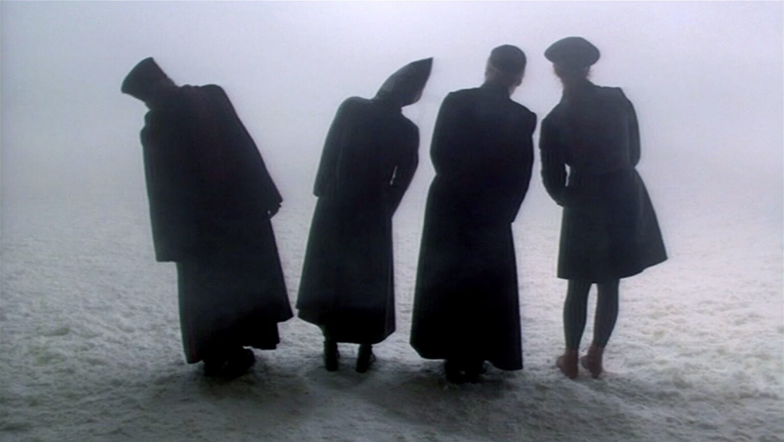 Photo en noir et blanc. Quatre personnes de dos, certains habillés en religieux, penchent la tête de côté et regardent quelque chose au loin que l'on ne voit pas.