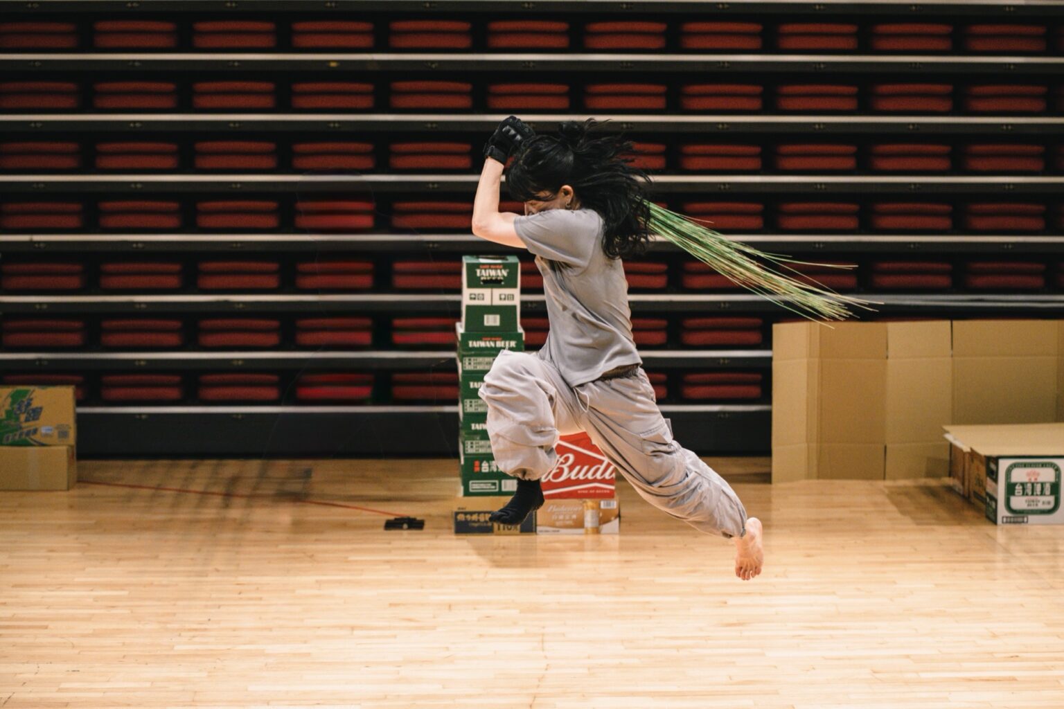 Une danseuse traverse la scène en sautant et porte à la main une plante, type roseaux.
