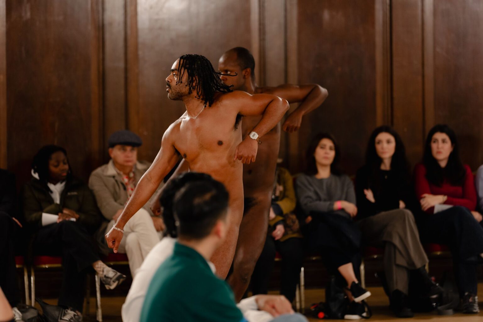 Deux personnes nues dansent au milieu d'une scène. On voit des spectateurs autour d'eux.