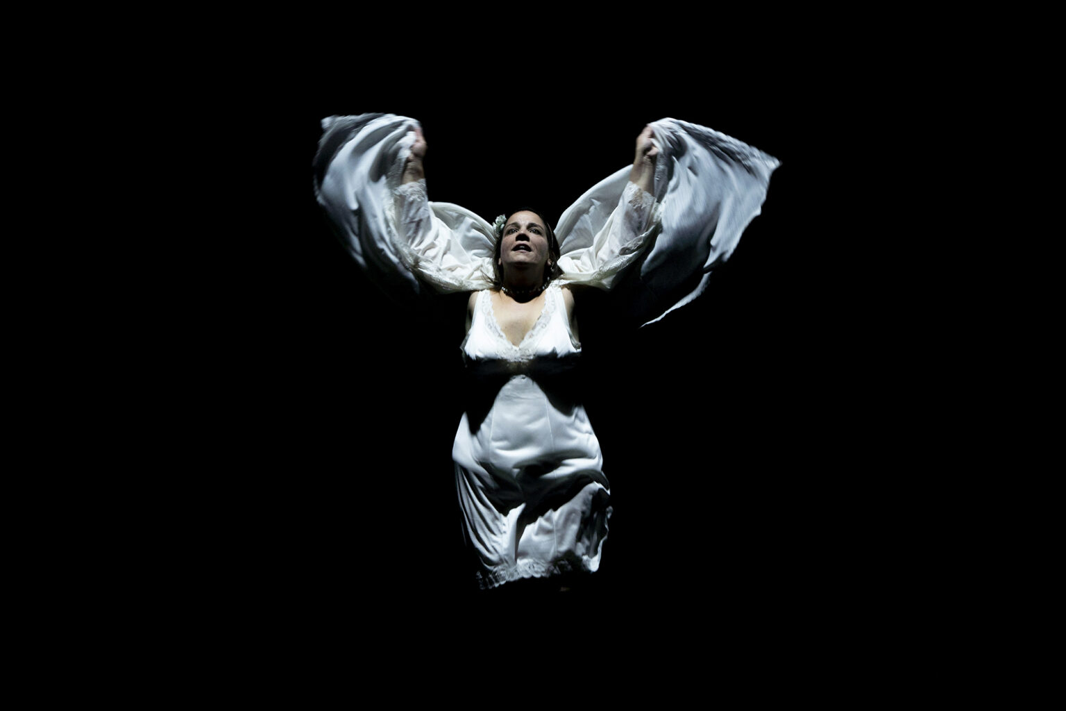 La comédienne en robe de chambre lève les bras et forme des ailes avec le tissus de son vêtement