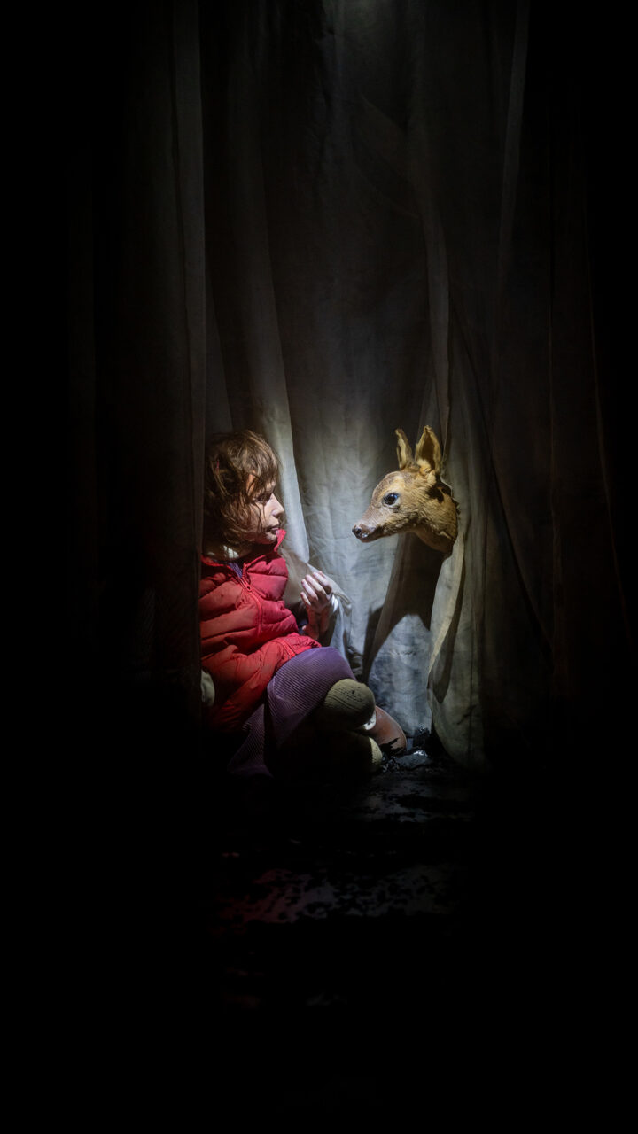 Une marionette d'enfant fait face à une biche dans une cabane de tissus