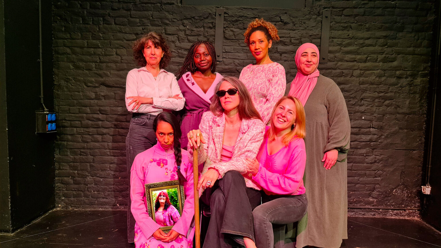 Photo avec les huit participantes de l'Atelier des Femmes. Trois sont devant assises, quatre autres sont derrière, debout. Elles portent des vêtements pour la plupart roses. L'une d'entre elles, absente lors de la séance photo, est représentée dans un cadre.