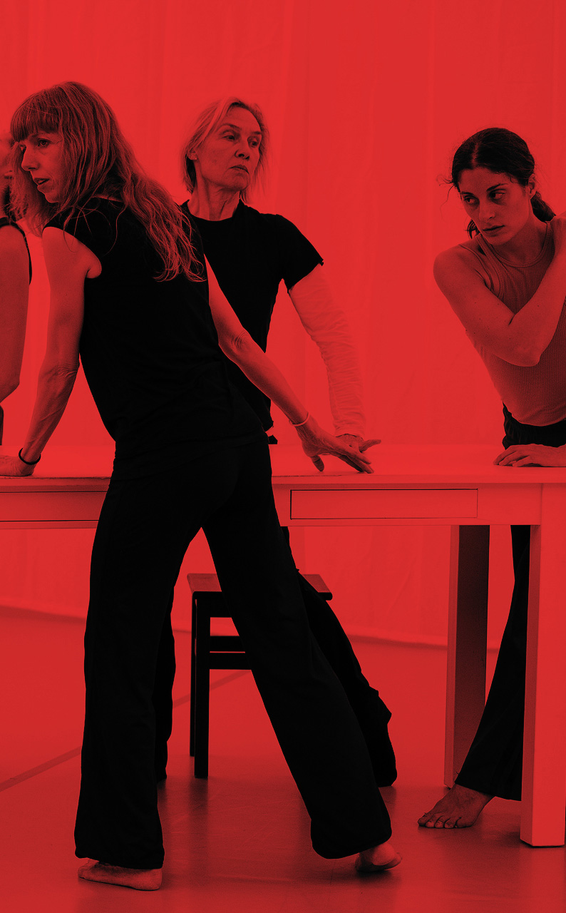 Trois danseuses de "Lignes de fracture" sont debout, autour d'une table. Elles portent un jogging et un t-shirt sombre. La photo est traitée avec un fond de couleur rouge intense.
