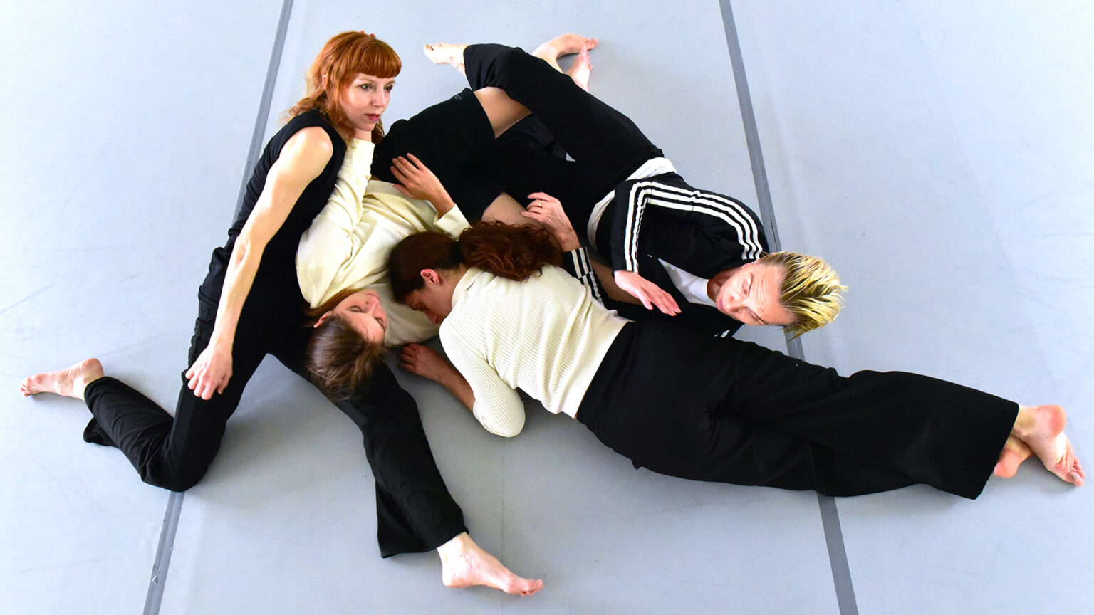 Les 4 interprètes de Lignes de fracture (Caterina Campo, Michèle Noiret, Lise Vachon, Léa Vinette) sont couchées sur un sol blanc. Leurs corps sont imbriqués les uns aux autres.