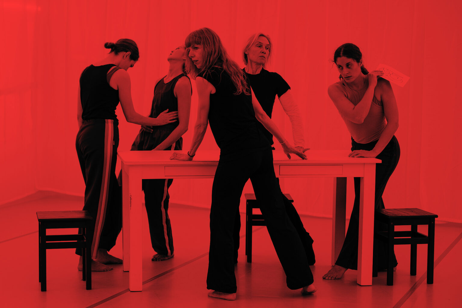 Les 5 danseuses de "Lignes de fracture" sont debout, autour d'une table. Elles portent un jogging et un t-shirt sombre. La photo est traitée avec un fond de couleur rouge intense.